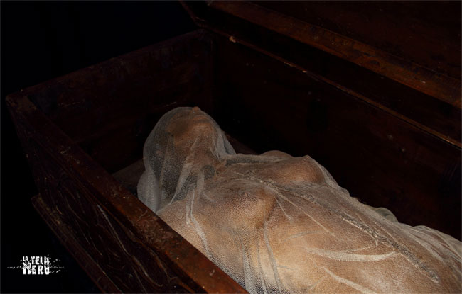 Cadavere post-autopsia avvolto in sudario all'interno di una bara